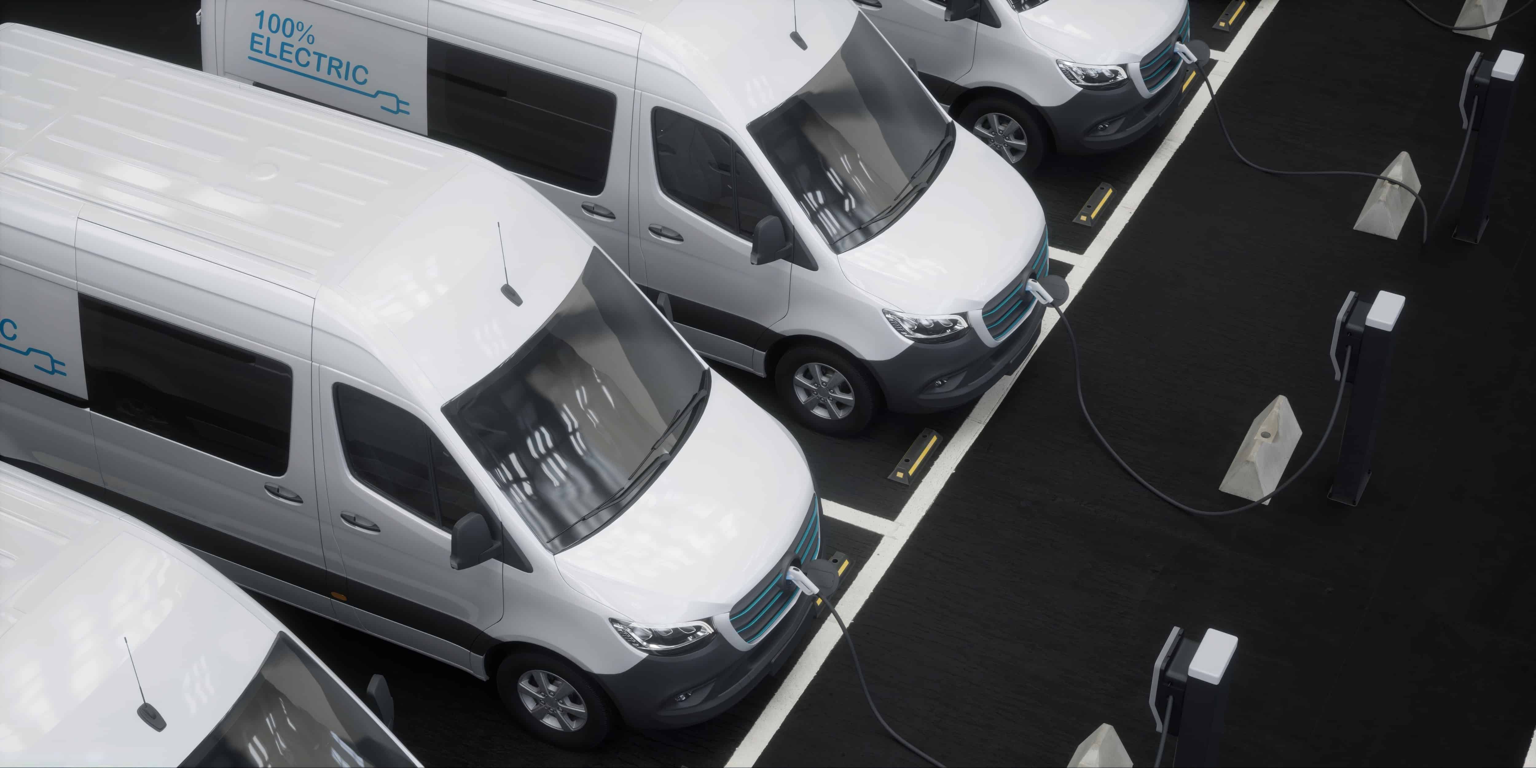 Fleet of generic electric EV delivery vans charging on charging stations